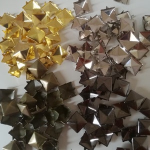 Peut inclure: Un tas de clous en métal en forme de pyramide de couleur or, argent et bronze. Les clous sont disposés en trois groupes, les clous dorés à gauche, les clous argentés au milieu et les clous bronze à droite.
