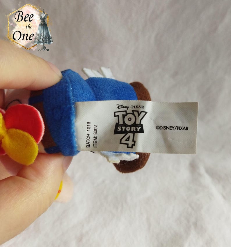 K&ouml;nnte beinhalten: Ein blaues Pl&uuml;schtier von Woody aus Toy Story 4. Das Spielzeug hat eine rote und gelbe Blume auf dem Kopf. Das Etikett auf dem Spielzeug lautet "Disney Pixar Toy Story 4" und "&copy;DISNEY/PIXAR".
