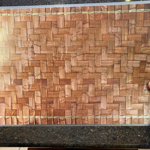 May include: Rectangular cutting board with a woven bamboo pattern. The board has a clear border and is held by a person's hand. The bamboo design features shades of brown and tan, creating a natural, textured appearance.