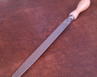 Puede incluir: Una lima de metal con mango de madera. La lima tiene forma rectangular con superficie texturizada y el número "2" estampado en el metal. El mango es de madera clara.
