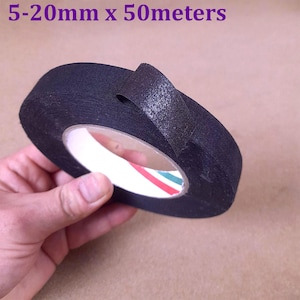 Peut inclure: Un rouleau de ruban isolant noir avec le texte "5-20mm x 50 mètres" en violet. Le ruban est tenu par une main et possède un cœur rayé rouge, blanc et bleu. Le ruban semble neuf et non utilisé.