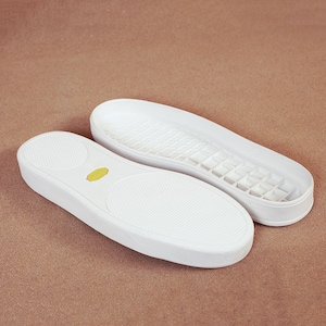 May include: Two white shoe insoles with textured surfaces and a yellow oval detail. One insole is upside down, revealing the patterned sole. The insoles are designed for sneakers or casual shoes.