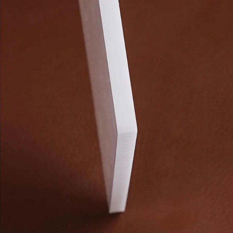May include: A white, rectangular object with a smooth surface, viewed from a side angle. The object has a clean, minimalist aesthetic, with a sharp edge and a solid, opaque appearance. The background is a solid brown color.