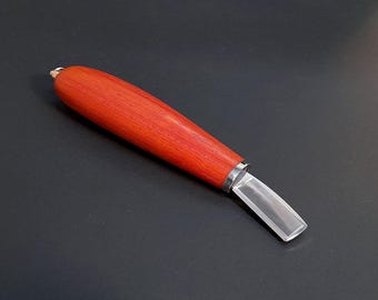 May include: A wood carving tool featuring a smooth, cylindrical, reddish-orange wooden handle with a visible grain pattern. The handle is attached to a short, flat, rectangular metal blade with a beveled edge and a polished, reflective finish.