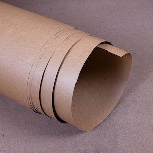 Può includere: Un rotolo di carta kraft marrone, arrotolato strettamente. Gli strati della carta sono visibili, con una consistenza liscia e una tonalità calda e terrosa. I bordi sono leggermente curvi. Lo sfondo è di un marrone simile, creando un aspetto coerente.