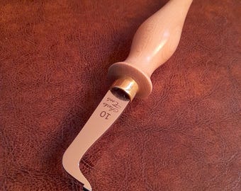 May include: A wooden handled leather working tool with a curved blade. The blade is engraved with "10" and "Saddle Tools".