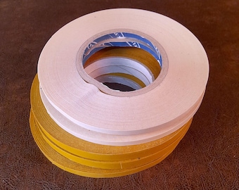 May include: A stack of adhesive tapes in white and gold. The rolls are neatly arranged, with the white tape on top and the gold tape at the bottom. The tape is on a brown surface.