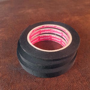 May include: A stack of black electrical tape rolls. The tape has a red inner core with the word "starbant" printed repeatedly. The tape is on a brown surface.