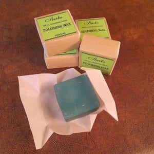 Puede incluir: Cuatro cajas pequeñas de cera para pulir metales Starko, con etiquetas verdes y el texto "POLISHING WAX". Una caja está abierta, revelando un bloque de cera verde sobre papel. Las cajas son marrones.