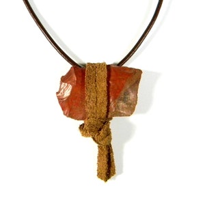 Könnte beinhalten: Ein roter Steinanhänger an einem braunen Lederband mit einem braunen Lederquaste.