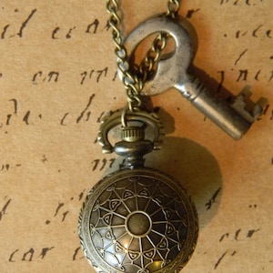 May include: A gold-toned necklace with a vintage pocket watch and a skeleton key pendant. The watch has a detailed, ornate design and the key is antique.