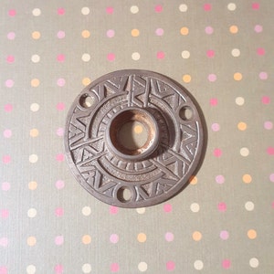 Pode incluir: Uma maçaneta de porta circular, adornada, de metal com um design decorativo e um furo central. A maçaneta é de cor bronze escuro.