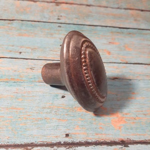 May include: A dark grey metal knob with a decorative beaded edge. The knob has a round top and a short stem.