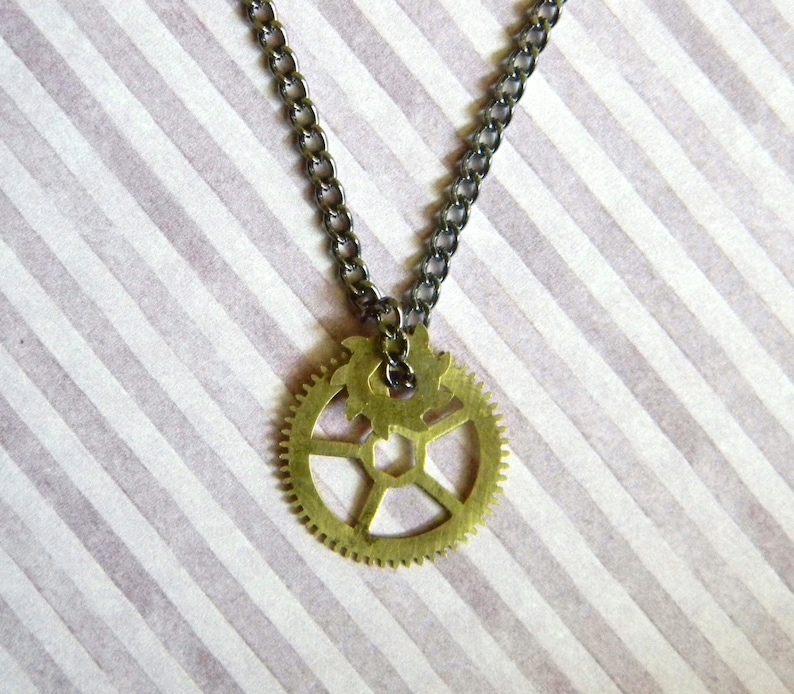 May include: A gold-toned necklace with a large, intricate gear pendant. The necklace is made of a silver chain.