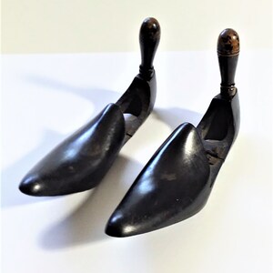 May include: Two wooden shoe trees with black polish and brown wooden knobs on top. The shoe trees are designed to help maintain the shape of shoes.