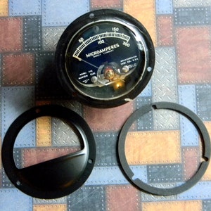 Puede incluir: Un medidor de microamperios anal&oacute;gico circular negro con una cara blanca y marcas negras. El medidor lee de 0 a 200 microamperios. El medidor est&aacute; etiquetado como "MICROAMPERES DIRECT CURRENT" y "MODEL 115 MARION ELEC."