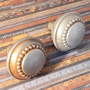 May include: Two silver and gold decorative door knobs with a beaded trim. The knobs are on a background of patterned paper with a steampunk theme.