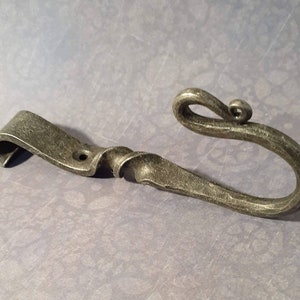 May include: A hand-forged metal hook with a twisted stem and a decorative curl at the end. The hook is made of a dark gray metal and has a rustic finish.