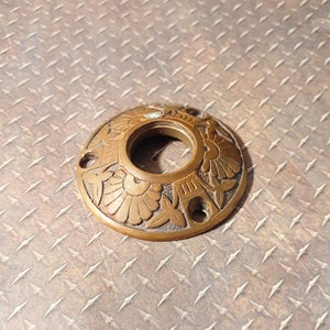 Pode incluir: Um botão de porta redondo de latão decorativo com um design floral intrincado.