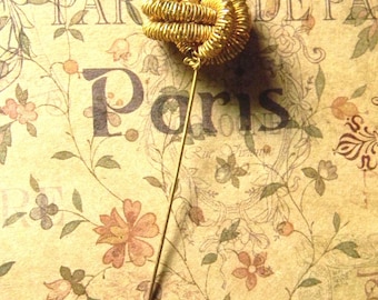 May include: A gold wire pin with a knot design. The pin is on a vintage background with the word "Paris" printed on it.