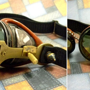 May include: A pair of steampunk goggles with brass accents and a black leather strap. The goggles have a magnifying lens on one side and a small telescope on the other.