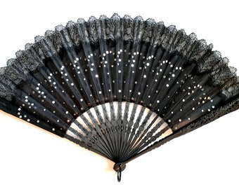 May include: A black lace fan with a black wooden handle and silver sequins. The fan is closed and has a scalloped edge.