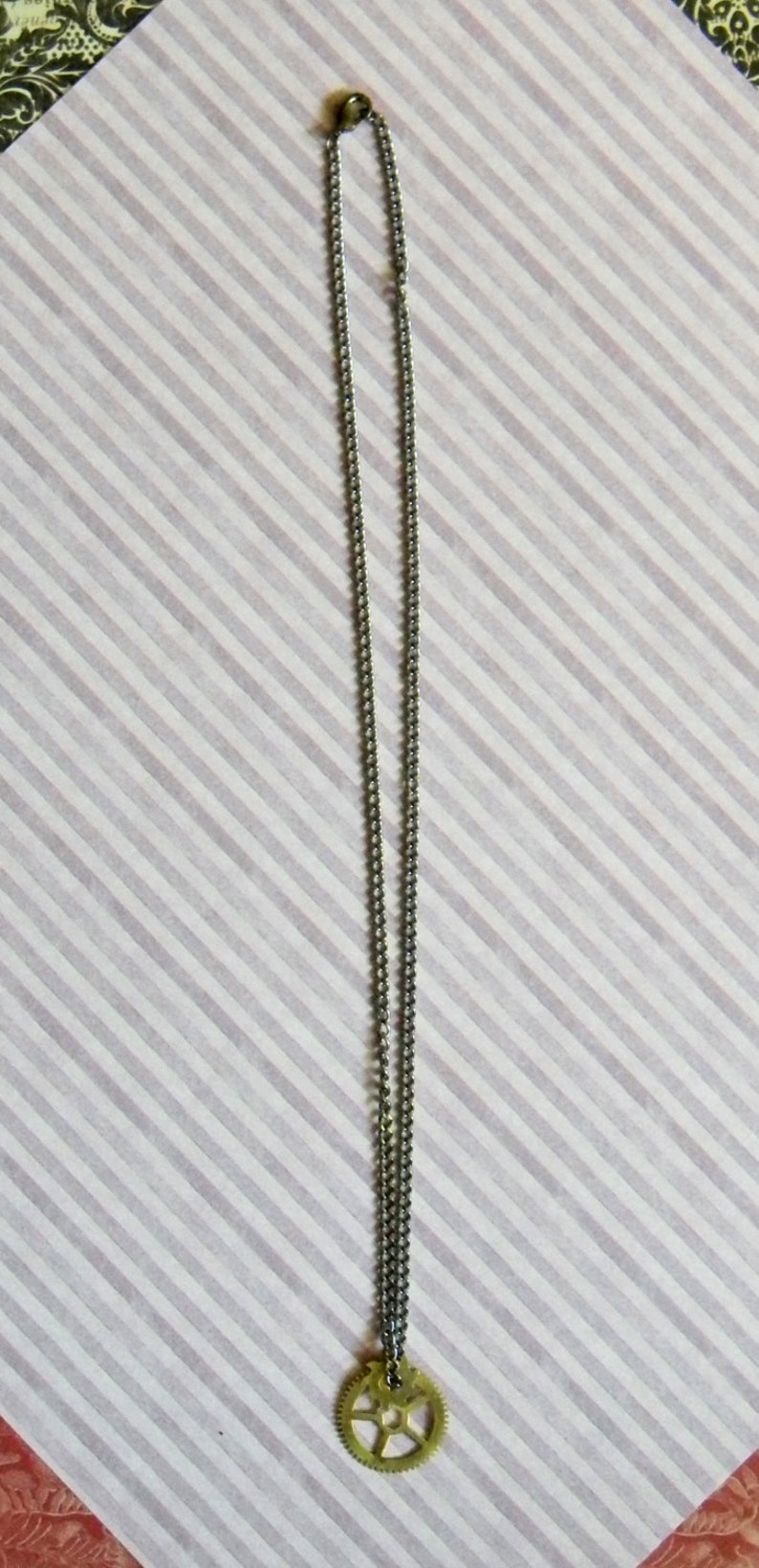 May include: A silver chain necklace with a gold gear pendant.