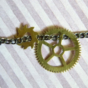 May include: A silver chain necklace with two brass gears, one large and one small. The large gear has a six-pointed star design.