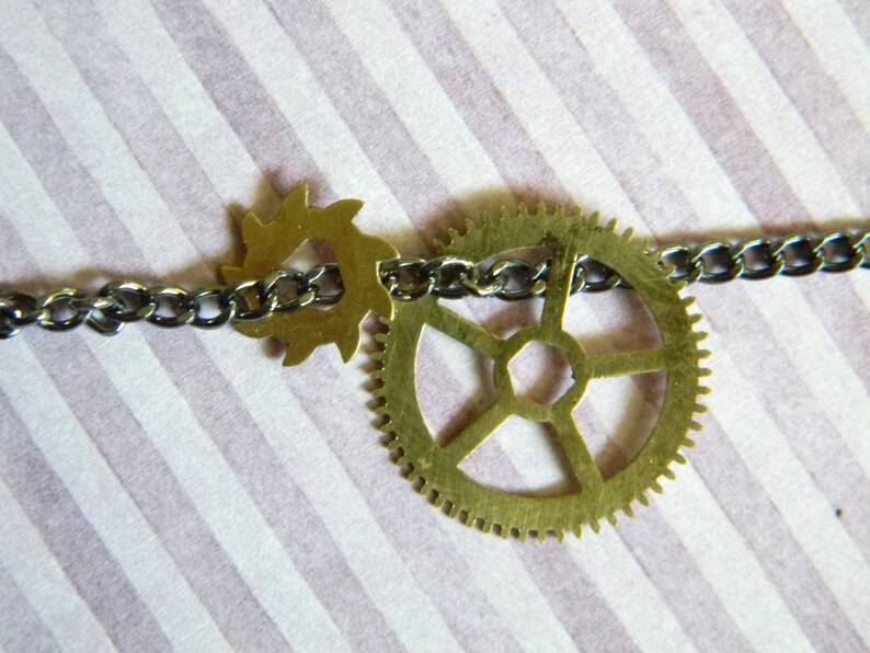 May include: A silver chain necklace with two brass gears, one large and one small. The large gear has a six-pointed star design.