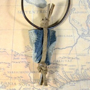 May include: A dark gray and brown stone pendant with a leather cord and brown leather tassels. The pendant is tied to the cord with a knot.