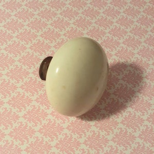 May include: White ceramic door knob with a brown metal base. The knob is round and has a smooth surface.