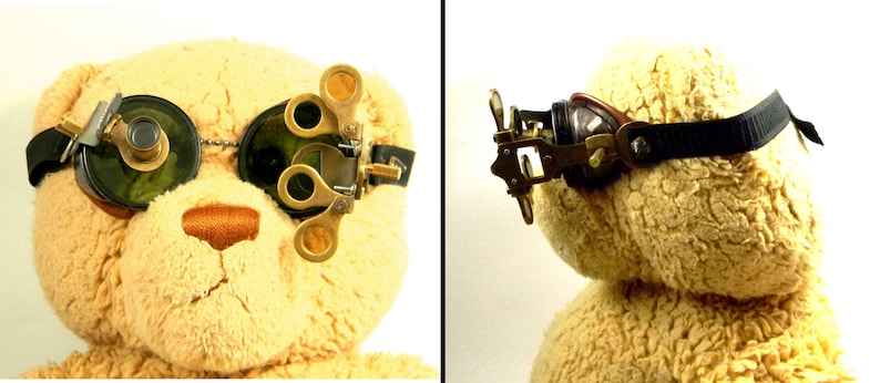 May include: A teddy bear wearing a pair of steampunk goggles with a magnifying lens on one side and a round lens on the other. The goggles are made of brass and have a black leather strap.