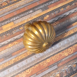 May include: A gold-toned, round, decorative cabinet knob with a ribbed design. The knob has a smooth, shiny finish.