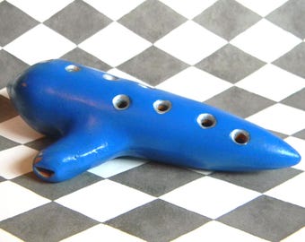 May include: A blue ceramic ocarina with six finger holes. The ocarina is a musical instrument that is played by blowing into a mouthpiece and covering the finger holes.