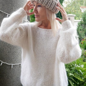 May include: A woman wearing a white knitted sweater and a beige knitted beanie hat.