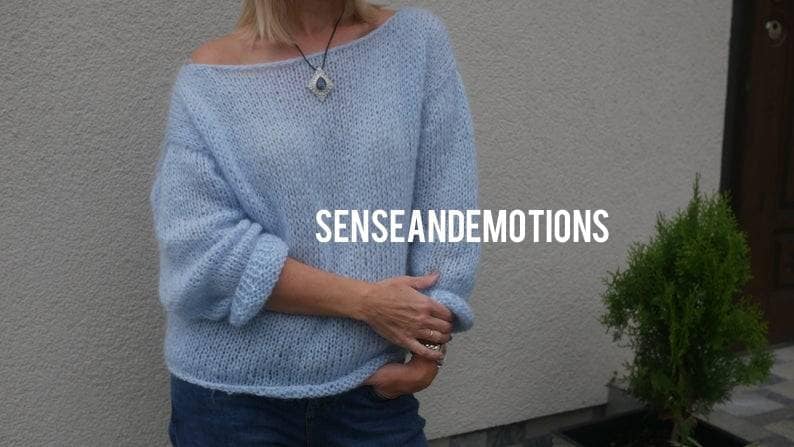 Op de afbeelding: Een lichtblauwe gebreide trui met een losse pasvorm en een licht off-shoulder halslijn. De trui is gemaakt van zacht, pluizig garen en heeft een ontspannen, casual stijl. De tekst "SENSEANDEMOTIONS" is zichtbaar op de trui.