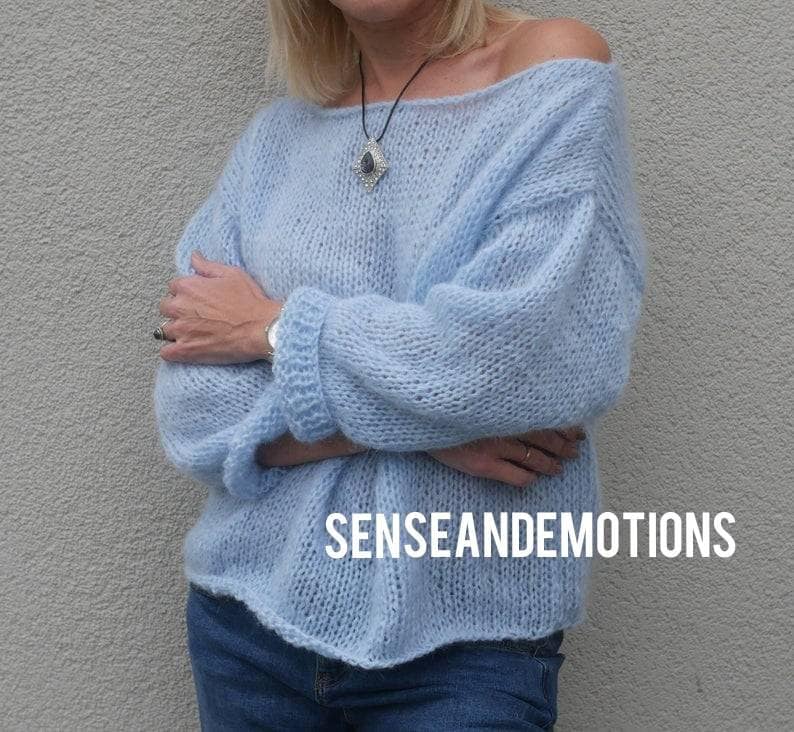 Op de afbeelding: Een lichtblauwe oversized gebreide trui met een losse pasvorm en lange mouwen. De trui heeft een brede halslijn en een ontspannen, casual stijl. De tekst "SENSEANDEMOTIONS" is zichtbaar aan de onderkant van de trui.