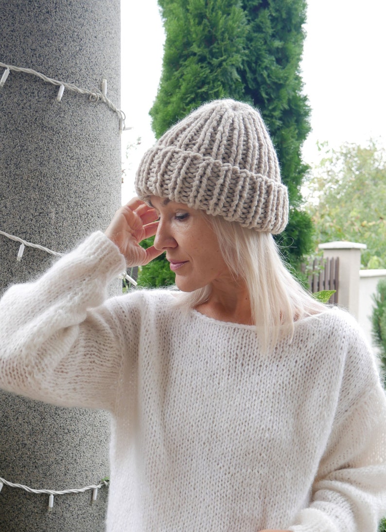 May include: A woman wearing a beige knitted beanie and a white knitted sweater.