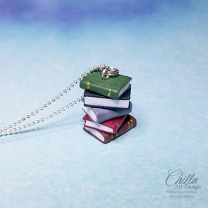 May include: A silver chain necklace with a charm of a stack of five miniature books. The books are green, black, grey, red, and brown. The charm is made of polymer clay.