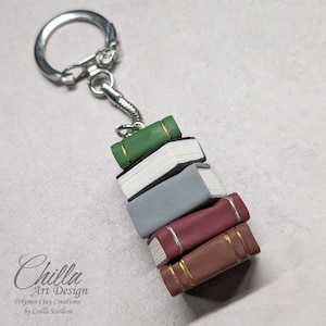 May include: A stack of five miniature books with gold accents on the covers. The books are green, white, gray, burgundy, and brown. The books are attached to a silver keychain.
