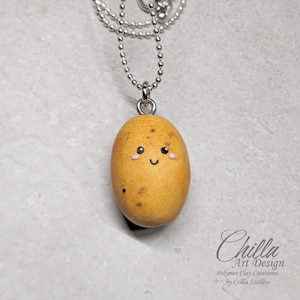 May include: A cute, smiling potato charm necklace made of polymer clay. The potato is brown and yellow with a simple, black smiley face and pink cheeks. The necklace is on a silver chain.