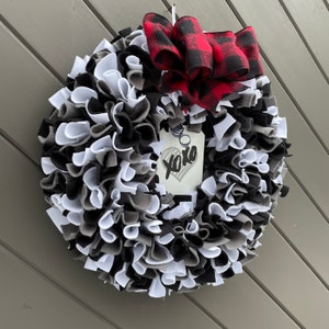 May include: A handmade wreath with a mix of black, white, and gray fabric strips. A red and black buffalo plaid bow is at the top. A tag with "xoxo" and a heart is attached.