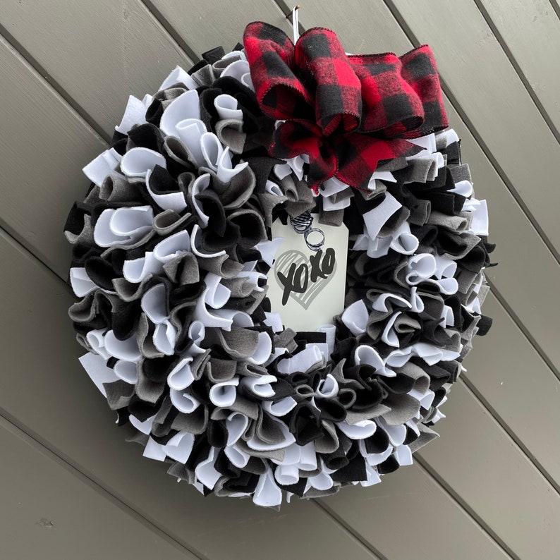 May include: A handmade wreath with a mix of black, white, and gray fabric strips. A red and black buffalo plaid bow is at the top. A tag with "xoxo" and a heart is attached.