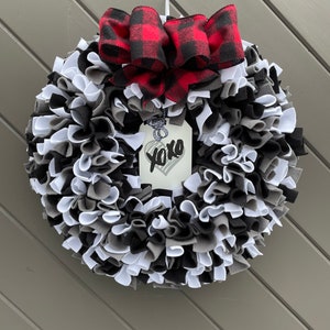 May include: A handmade wreath with a mix of black, white, and gray fabric strips. A red and black buffalo plaid bow sits at the top. A tag with "xoxo" and a heart hangs in the center.