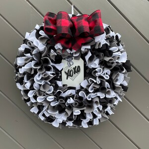 May include: A handmade wreath with a mix of black, white, and gray fabric strips. A red and black buffalo plaid bow sits at the top. A tag with a heart and the word "xoxo" hangs in the center.
