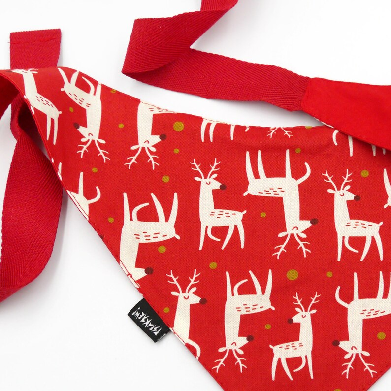 May include: Red bandana with a white reindeer pattern and gold polka dots. The bandana has a red ribbon tie.