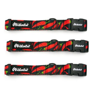 Puede incluir: Tres collares de perro negros con estampado de chile rojo y hebillas ajustables negras. Los collares tienen el texto "Primal Pet" impreso en ellos.