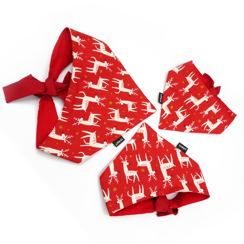 May include: Three red and white dog bandanas with a reindeer pattern. The bandanas are tied with a bow and have the word "Bark" printed on them.
