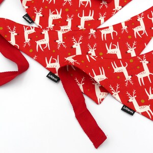 May include: Two red fabric dog bandanas with a white reindeer pattern and gold dots. The bandanas have a red ribbon attached and the word "remarkable" printed on the tag.