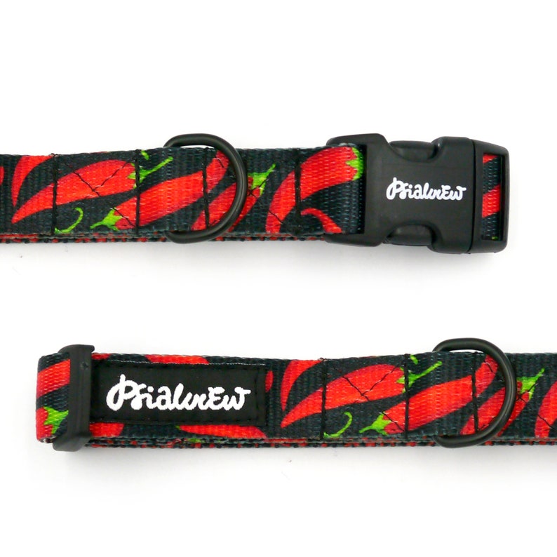 Puede incluir: Un collar de perro negro con estampado de chiles rojos y verdes. El collar tiene una hebilla negra con el texto "Primal Pet" en &eacute;l.
